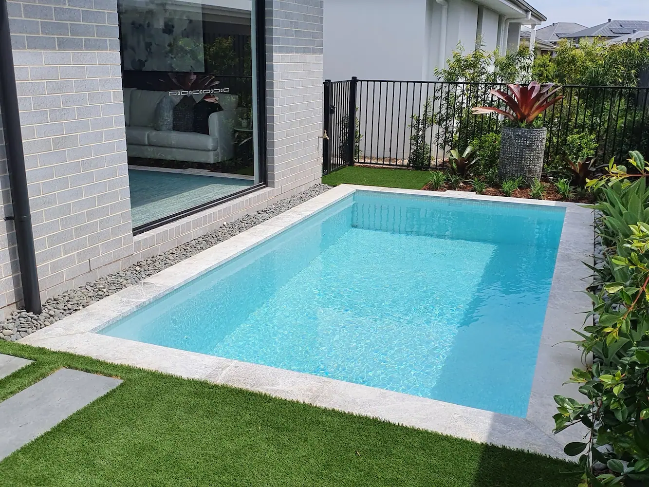 A plunge pool running along a rendered block wall, with artificial lawn up to the stone coping and a sliding door reflecting the water.